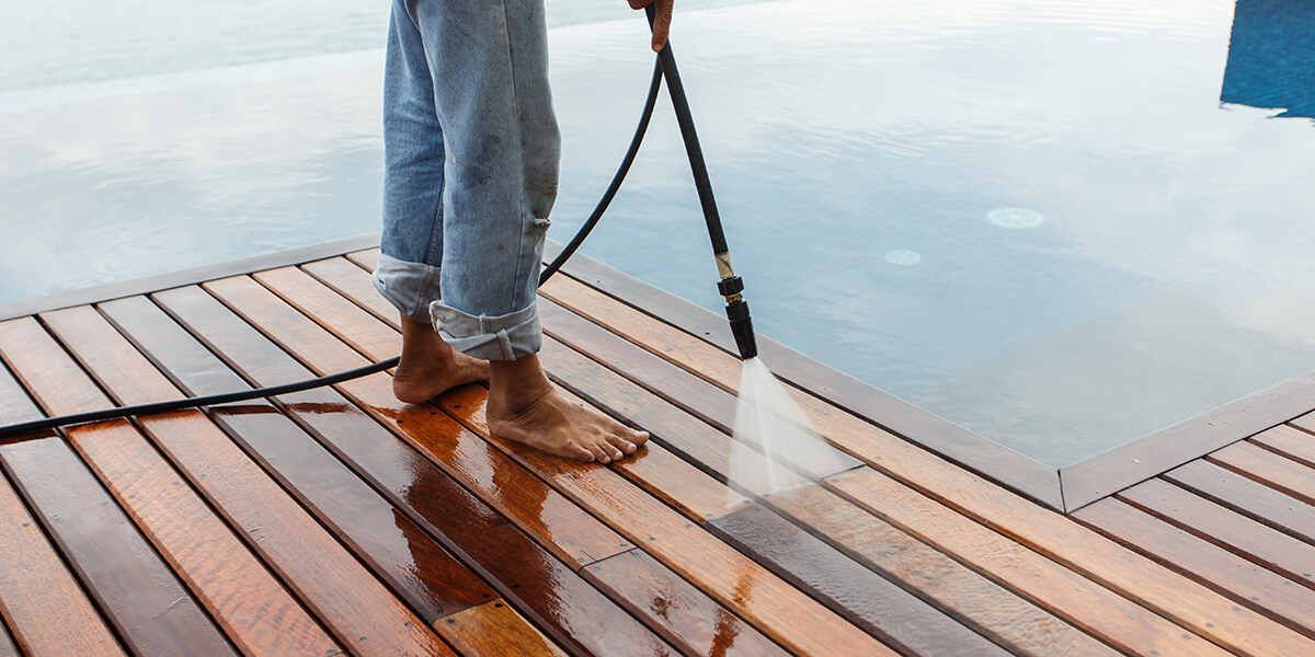 Person pressure washing a wooden deck next to a pool.