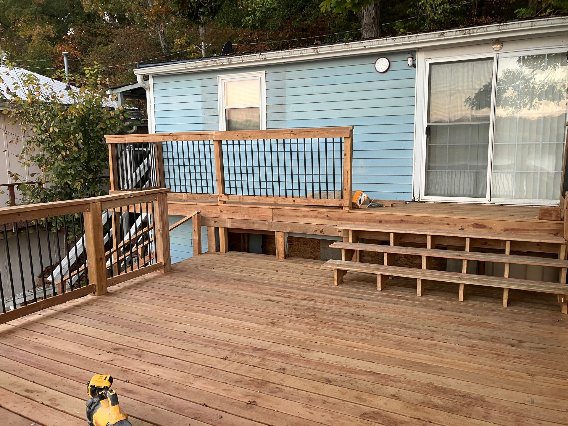 Wooden deck with steps leading to a blue house with a sliding glass door and window.
