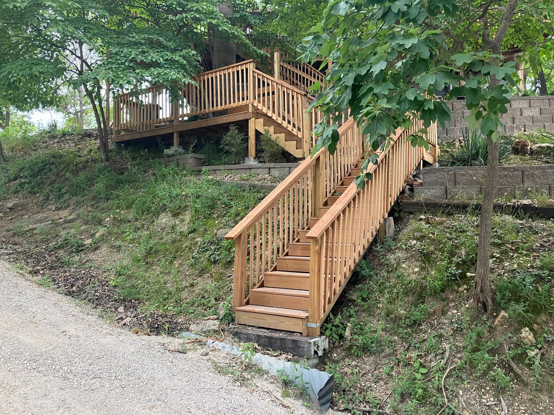 Wooden stairs and deck on a hillside, surrounded by trees and gravel path.