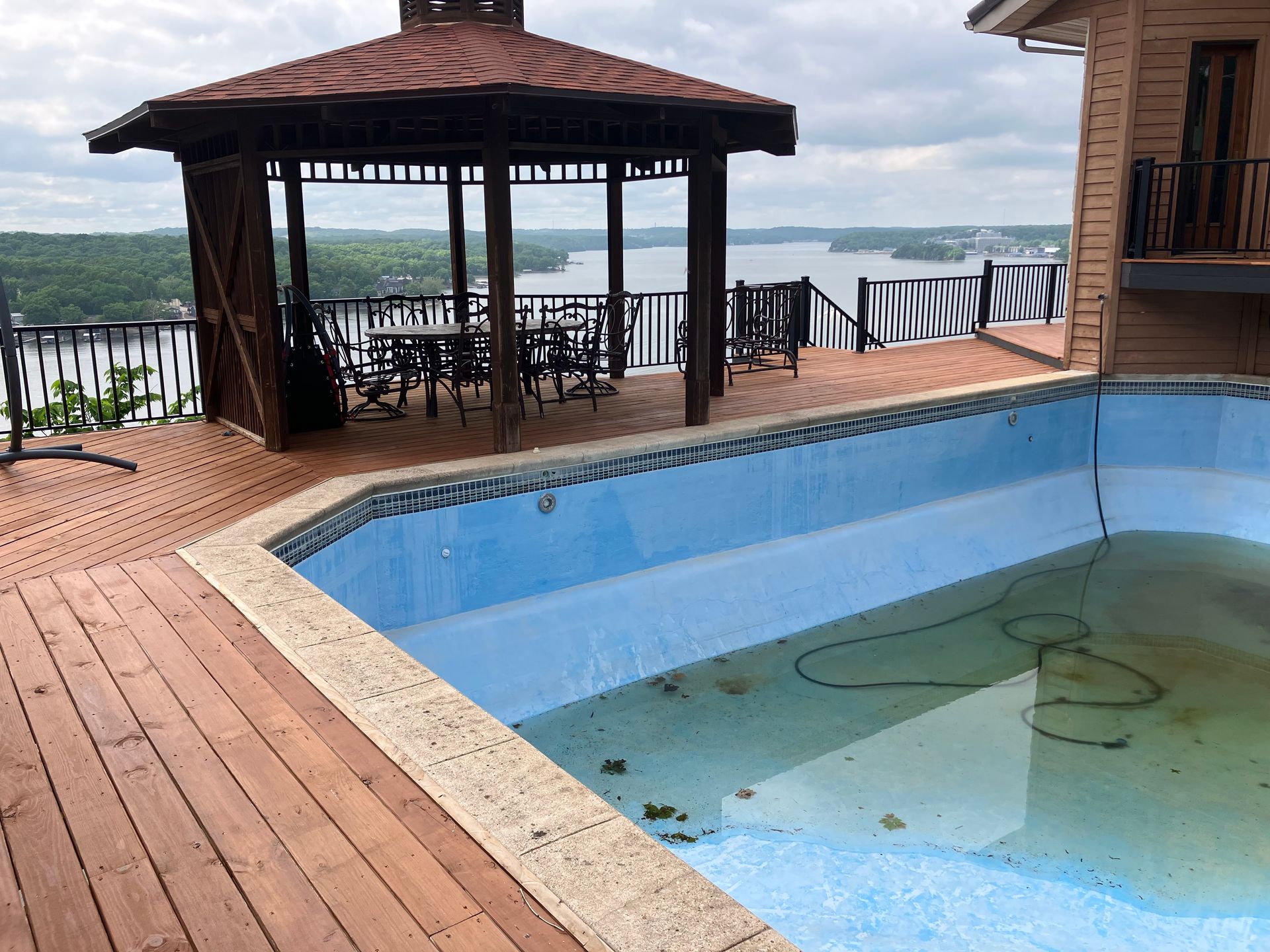 Empty pool with deck and gazebo overlooking a lake.