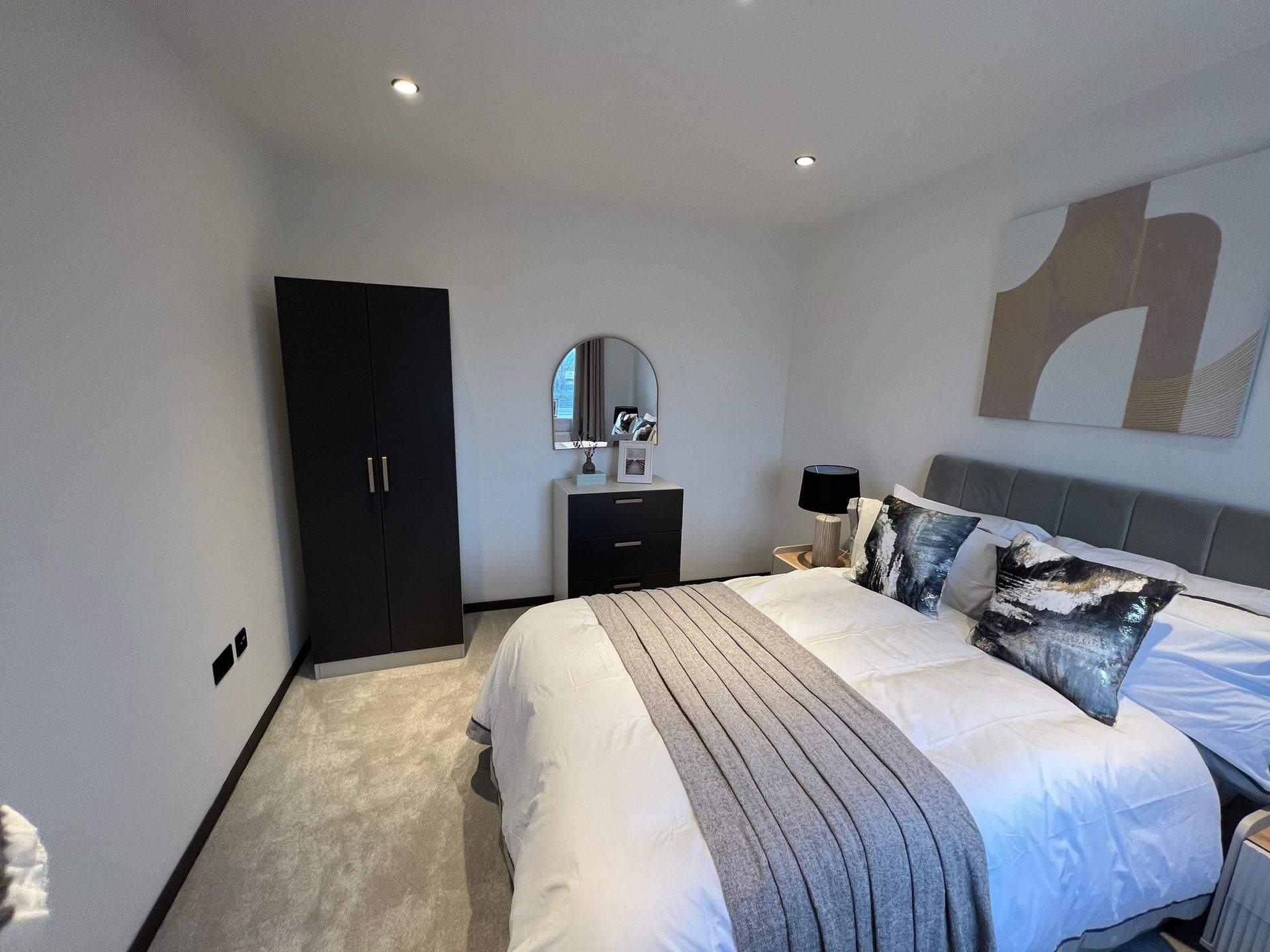 Bedroom with bed, dark wardrobe, vanity, and abstract art on the wall.