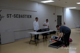 Trois hommes se tiennent autour d'une table dans une pièce avec un panneau indiquant Saint-Sébastien.