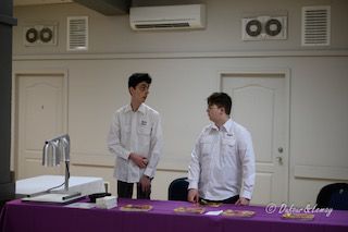 Deux hommes se tiennent l'un à côté de l'autre à une table dans une pièce.