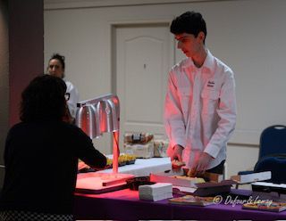 Un homme en chemise blanche prépare de la nourriture pour une femme à une table.