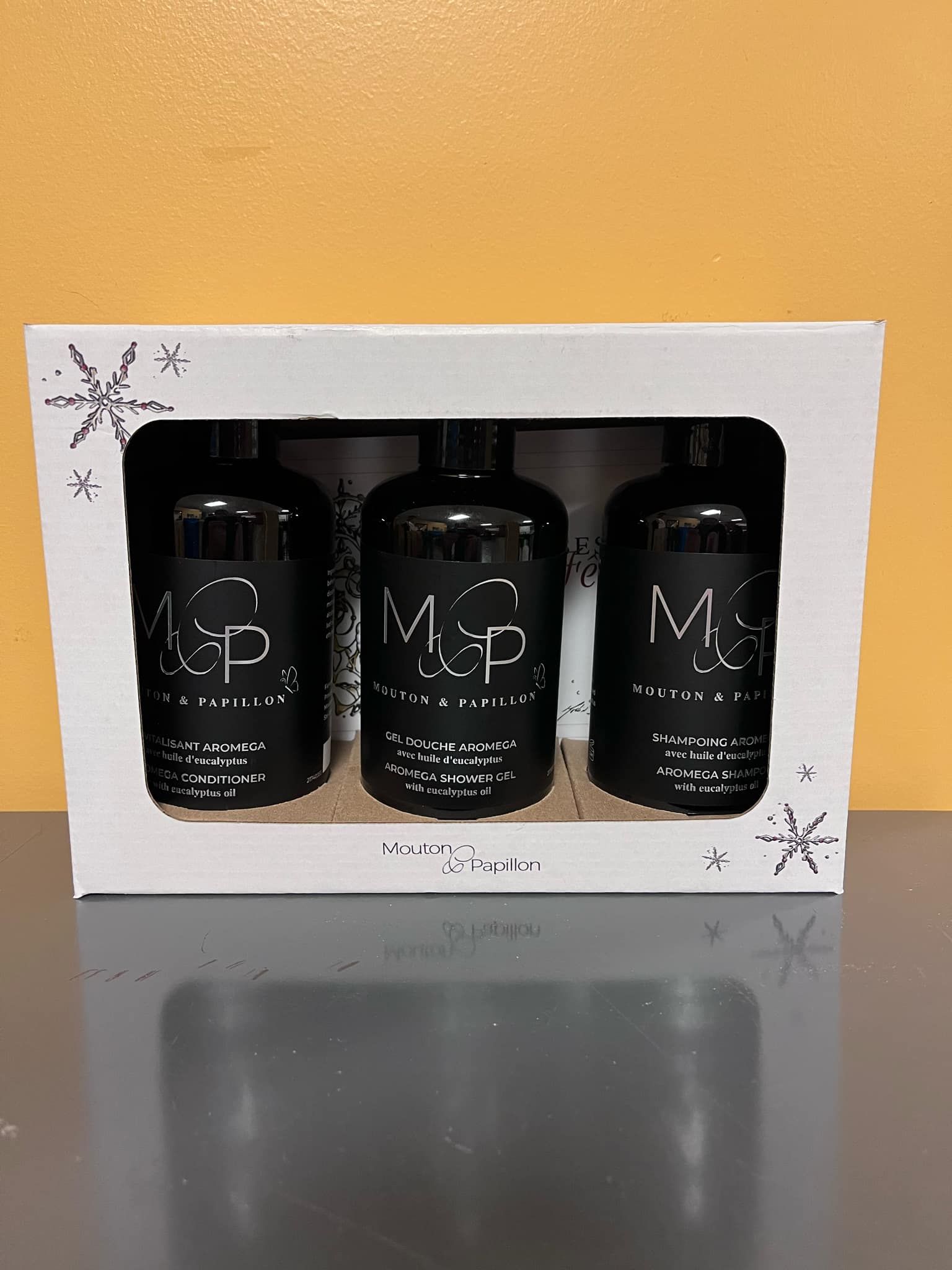 Trois bouteilles noires de shampoing sont dans une boîte blanche.