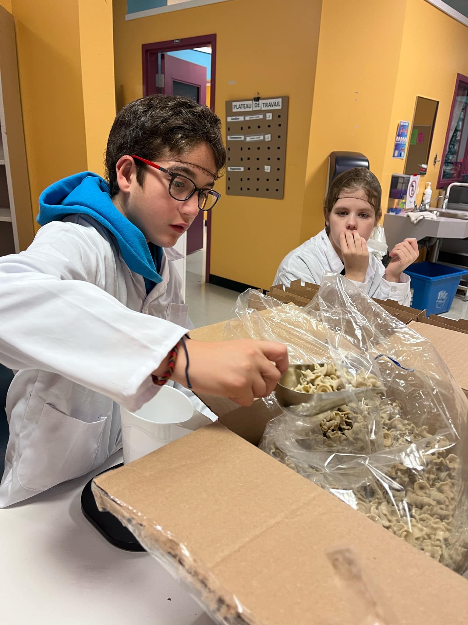 Un garçon en blouse de laboratoire ouvre une boîte de nourriture.