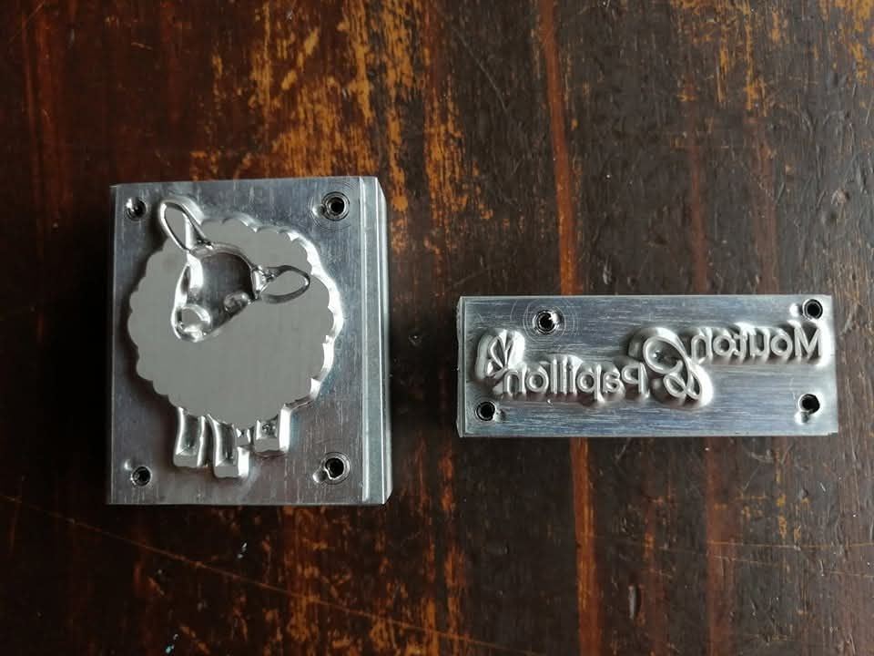 Deux timbres en métal avec un mouton dessus sont posés sur une table en bois.