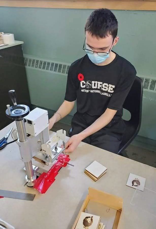 Un homme portant un masque est assis à une table et travaille sur une machine.