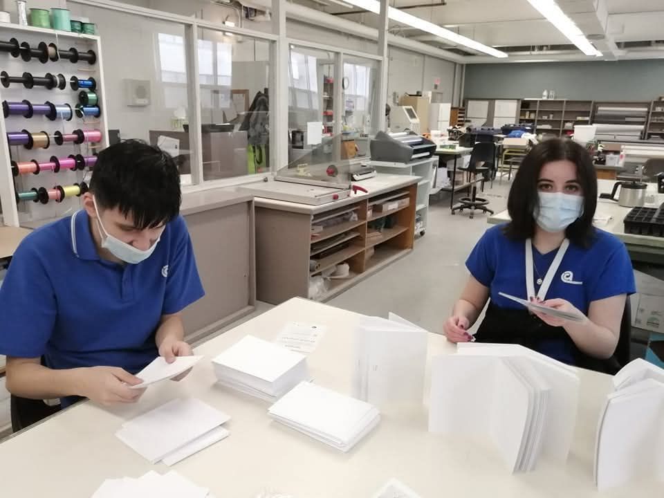 Un homme et une femme portant des masques sont assis à une table dans une usine.