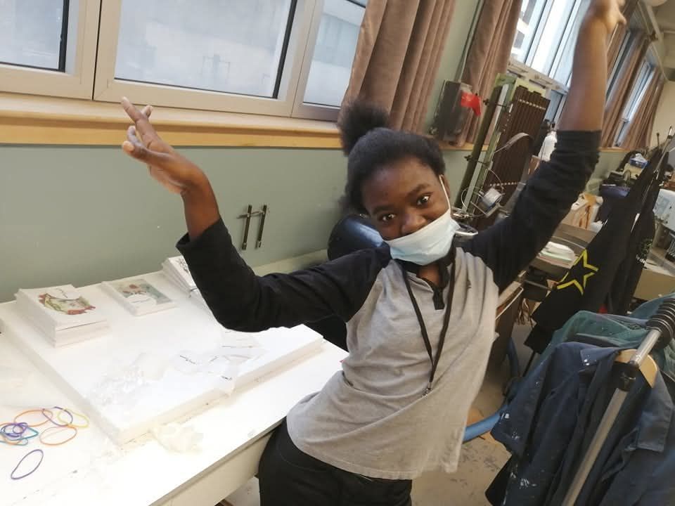Une femme portant un masque se tient devant une table avec les bras en l'air.