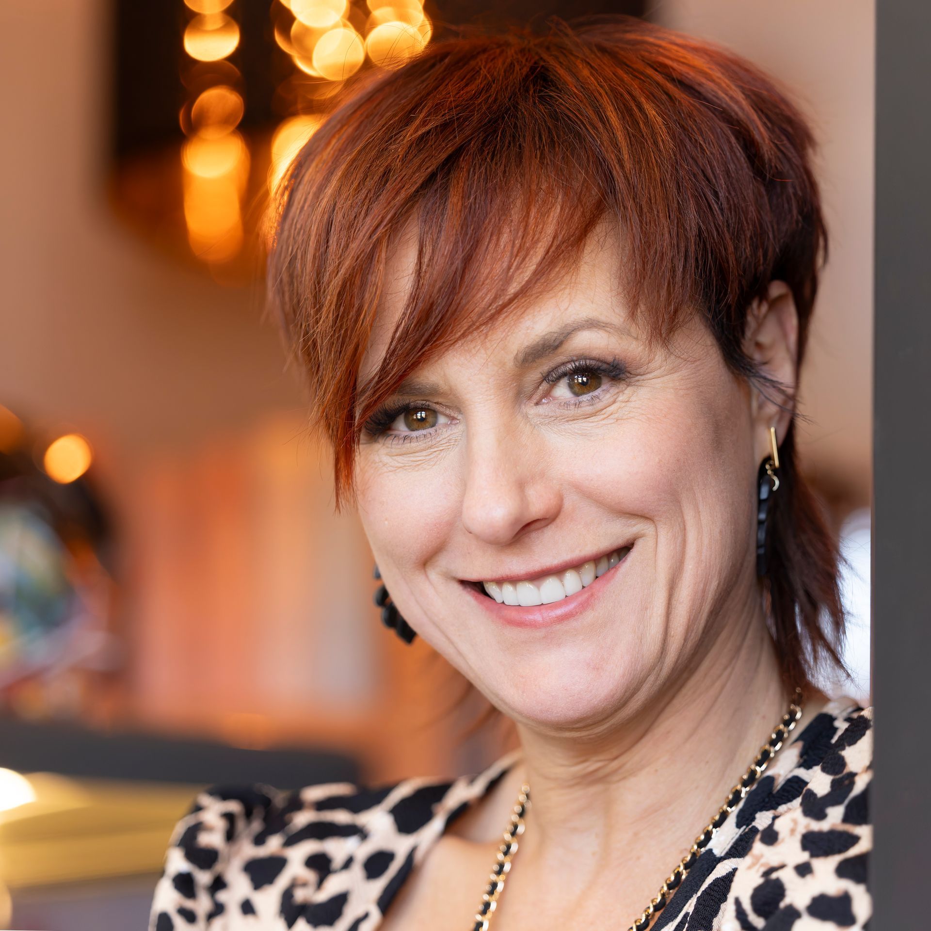 Une femme aux cheveux roux sourit et porte une veste à imprimé léopard