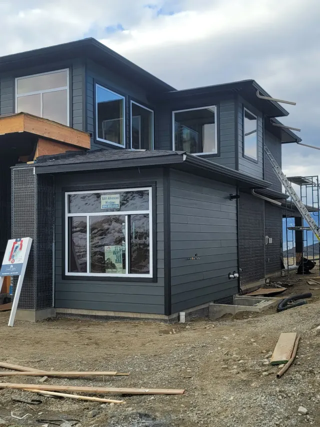 Exterior view of house with dark gray siding, white trim, and gutters against a blue sky.