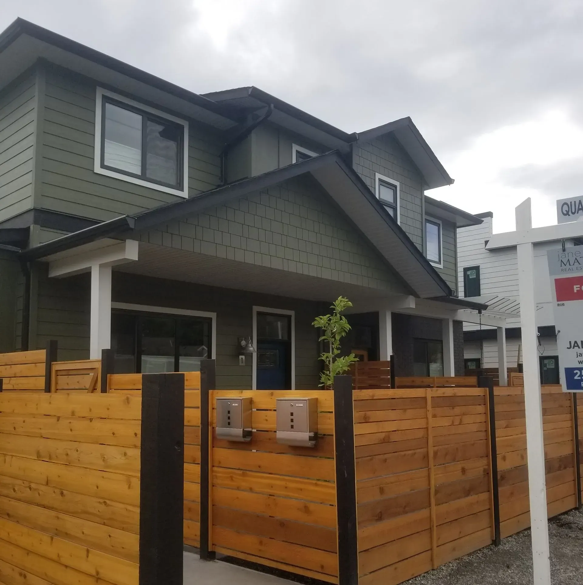 Modern house under construction with dark gray siding, white window frames, and debris in the foreground.