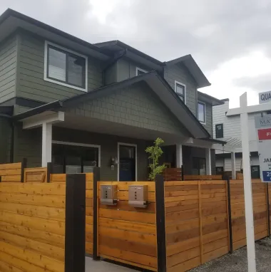 Green and brown townhouses with a wooden fence and a for-sale sign.