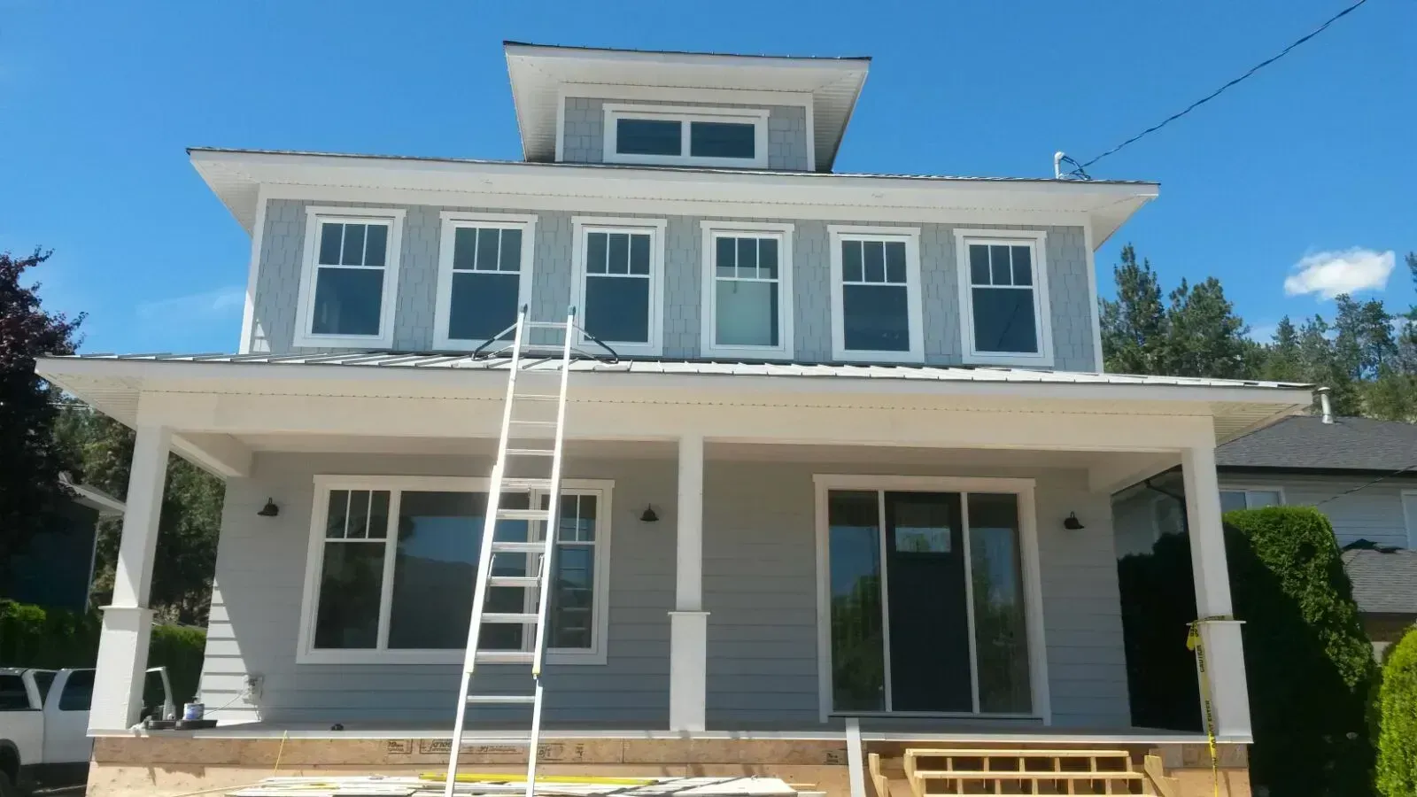 Exterior view of house with dark gray siding, white trim, and gutters against a blue sky.