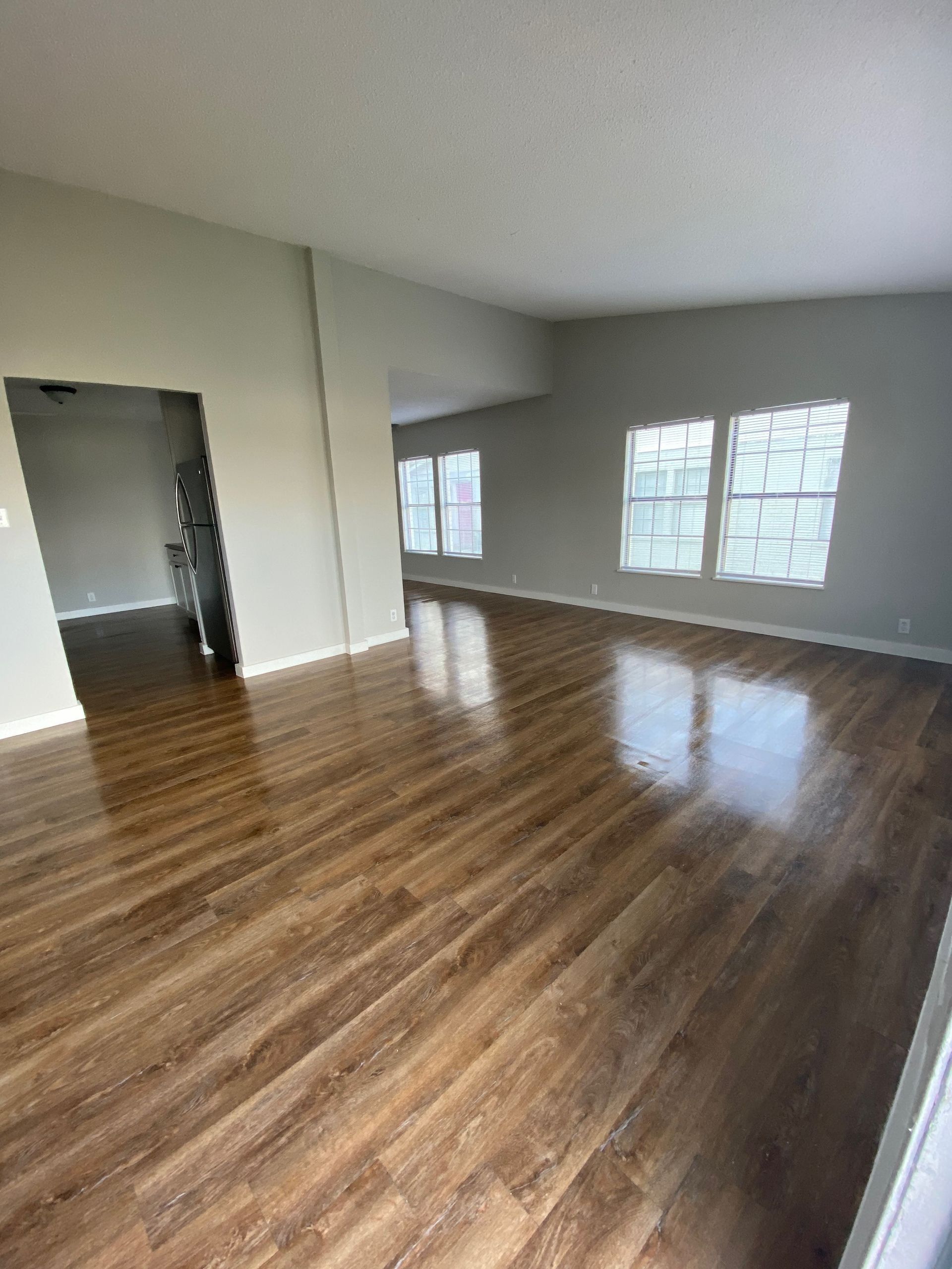 An empty living room with hardwood floors and lots of windows.