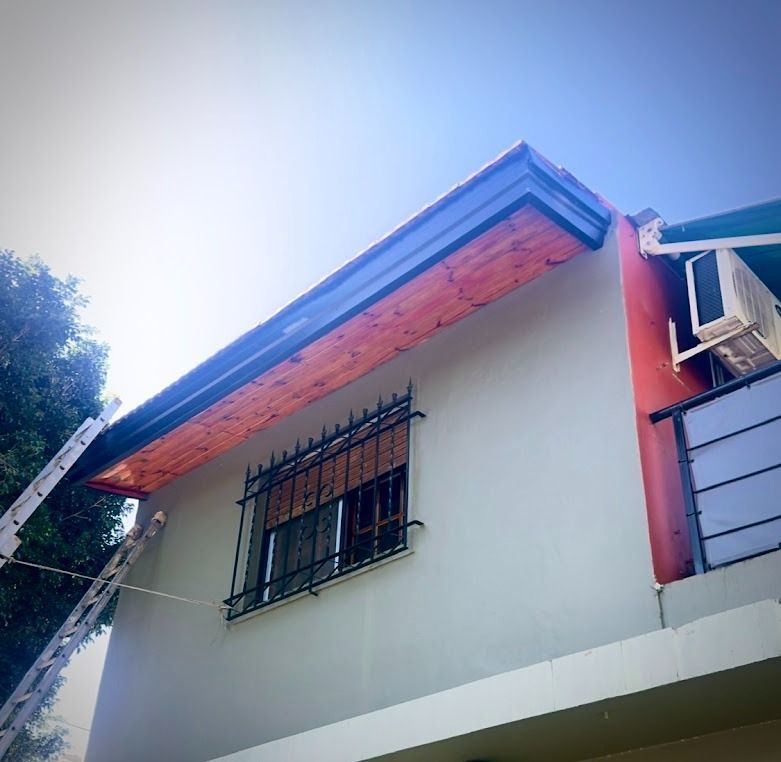 Exterior de una casa blanca con techo rojo, ventana enrejada y cielo azul brillante arriba.