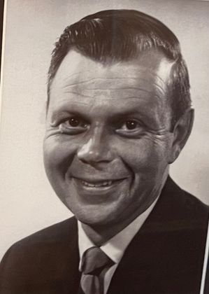 A black and white photo of a man in a suit and tie smiling.