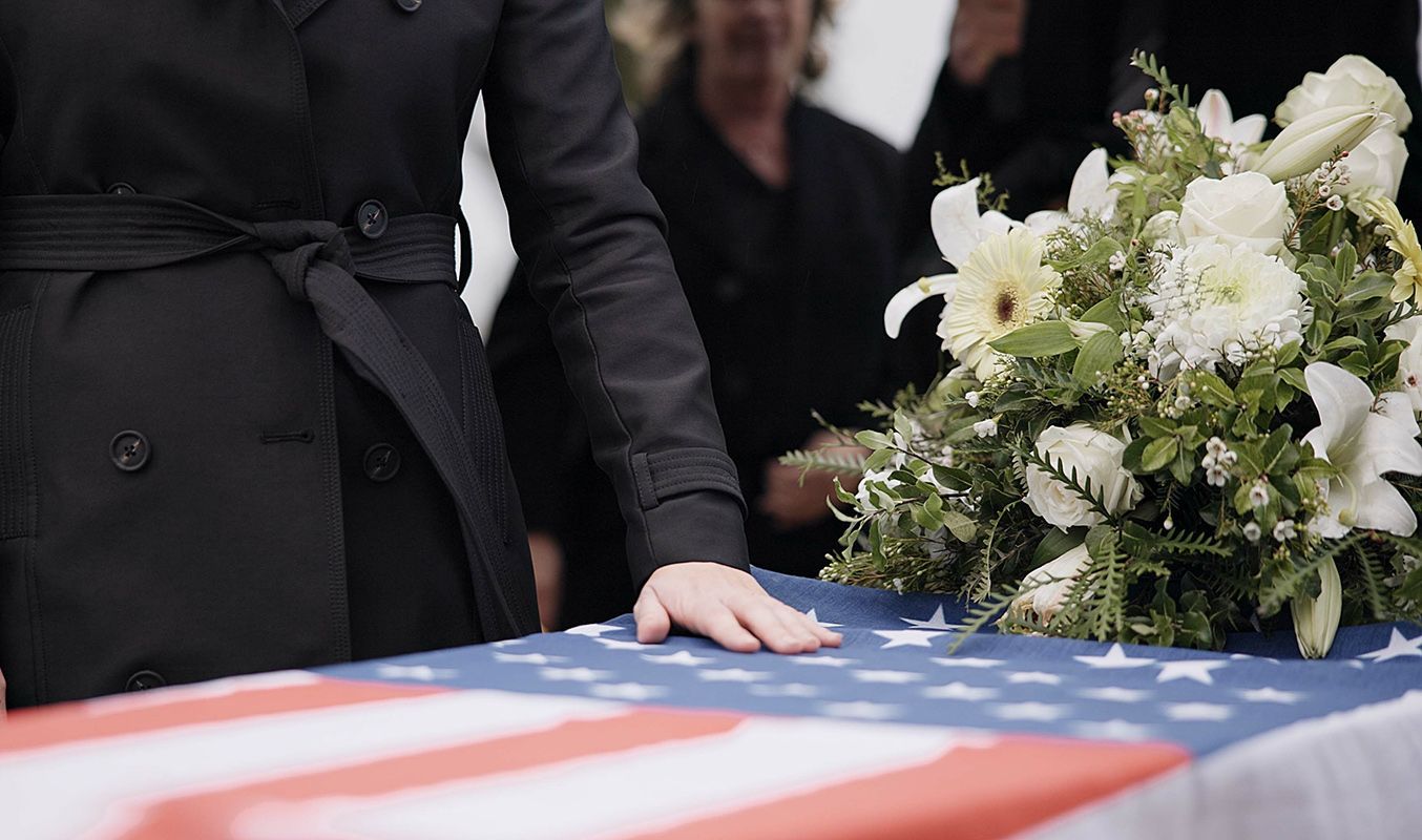 A woman is laying her hand on an american flag at a funeral.