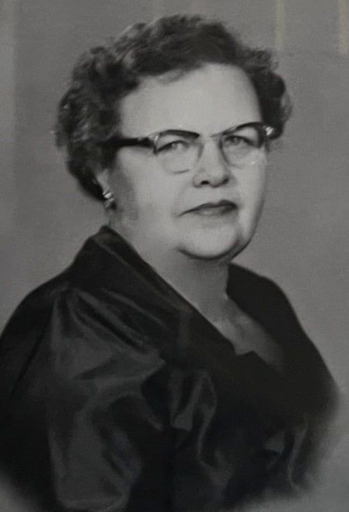 A black and white photo of an older woman wearing glasses and a black dress.
