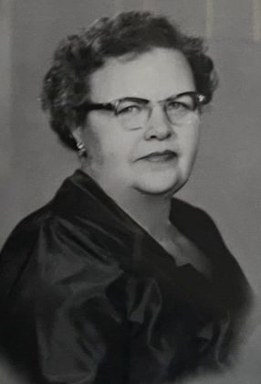 A black and white photo of an older woman wearing glasses and a black dress.
