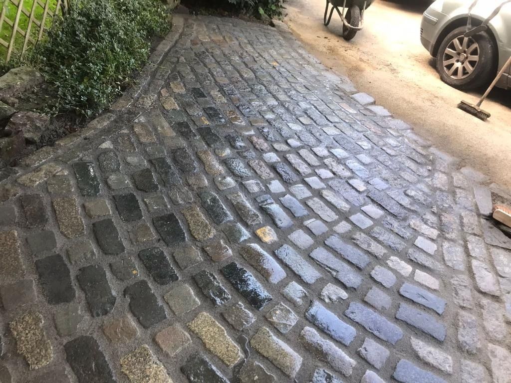 A car is parked on the side of a cobblestone driveway.