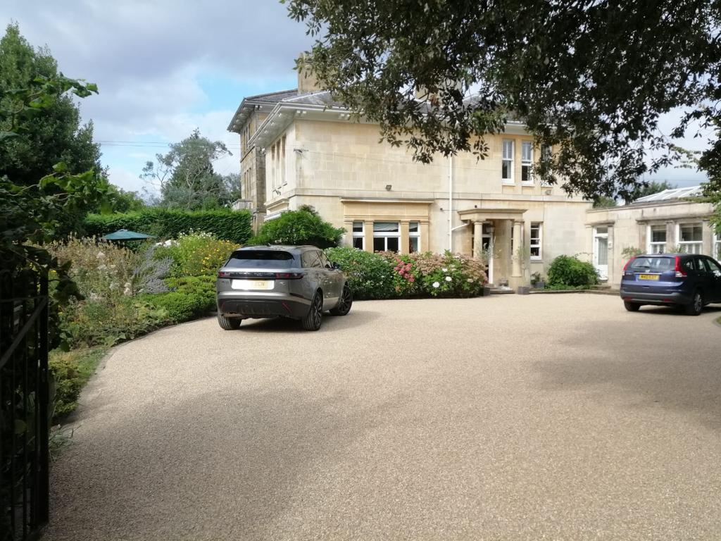 Two cars are parked in front of a large house tar & chip driveway 