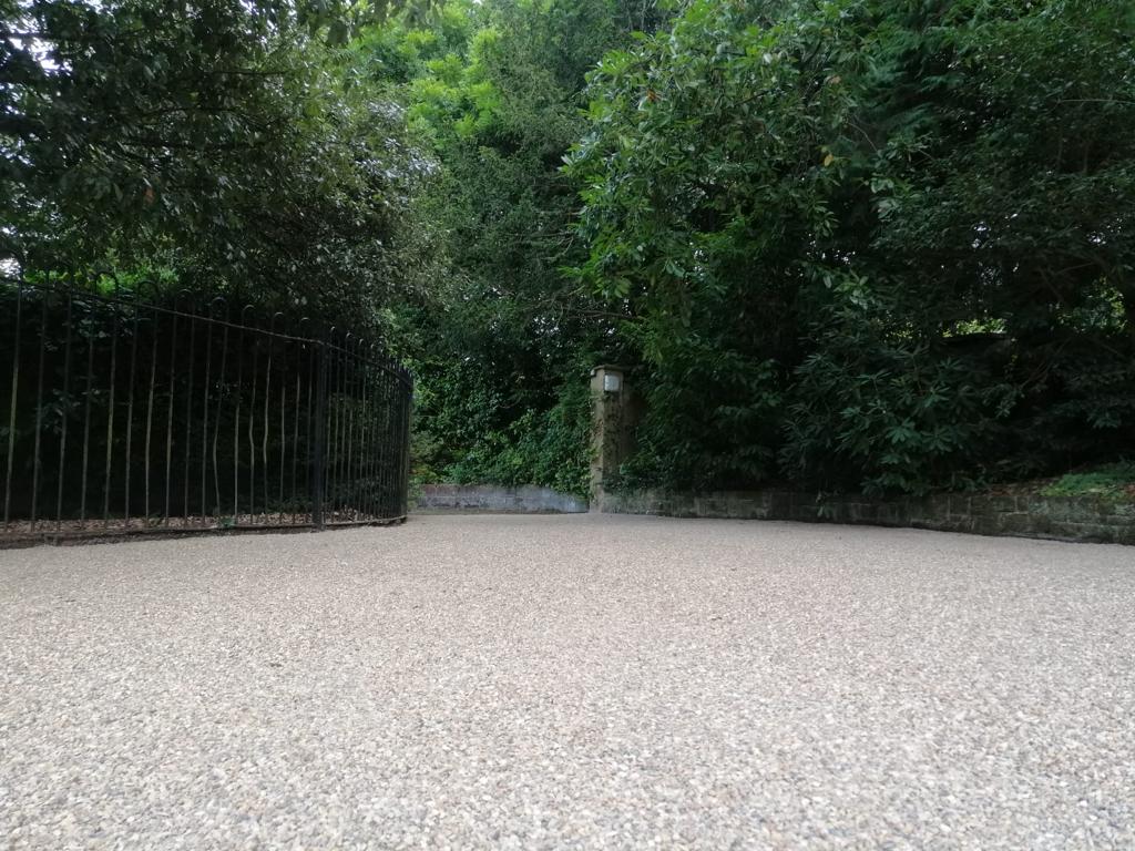 A gravel driveway with a fence and trees in the background.