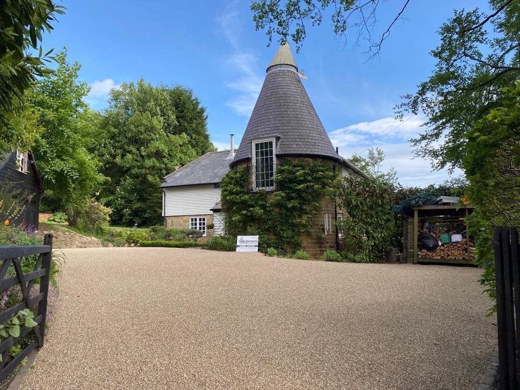 A large house with a cone shaped roof is surrounded by trees and tar & gravel driveway 