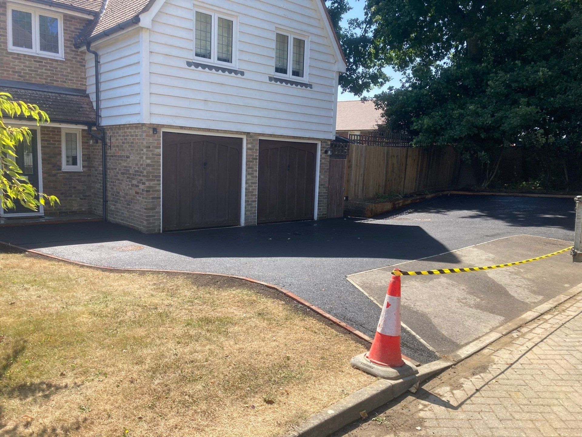 A house with a driveway and a traffic cone in front of it with black tarmac driveway.