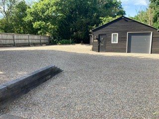 A black garage with a gray door and a gravel driveway