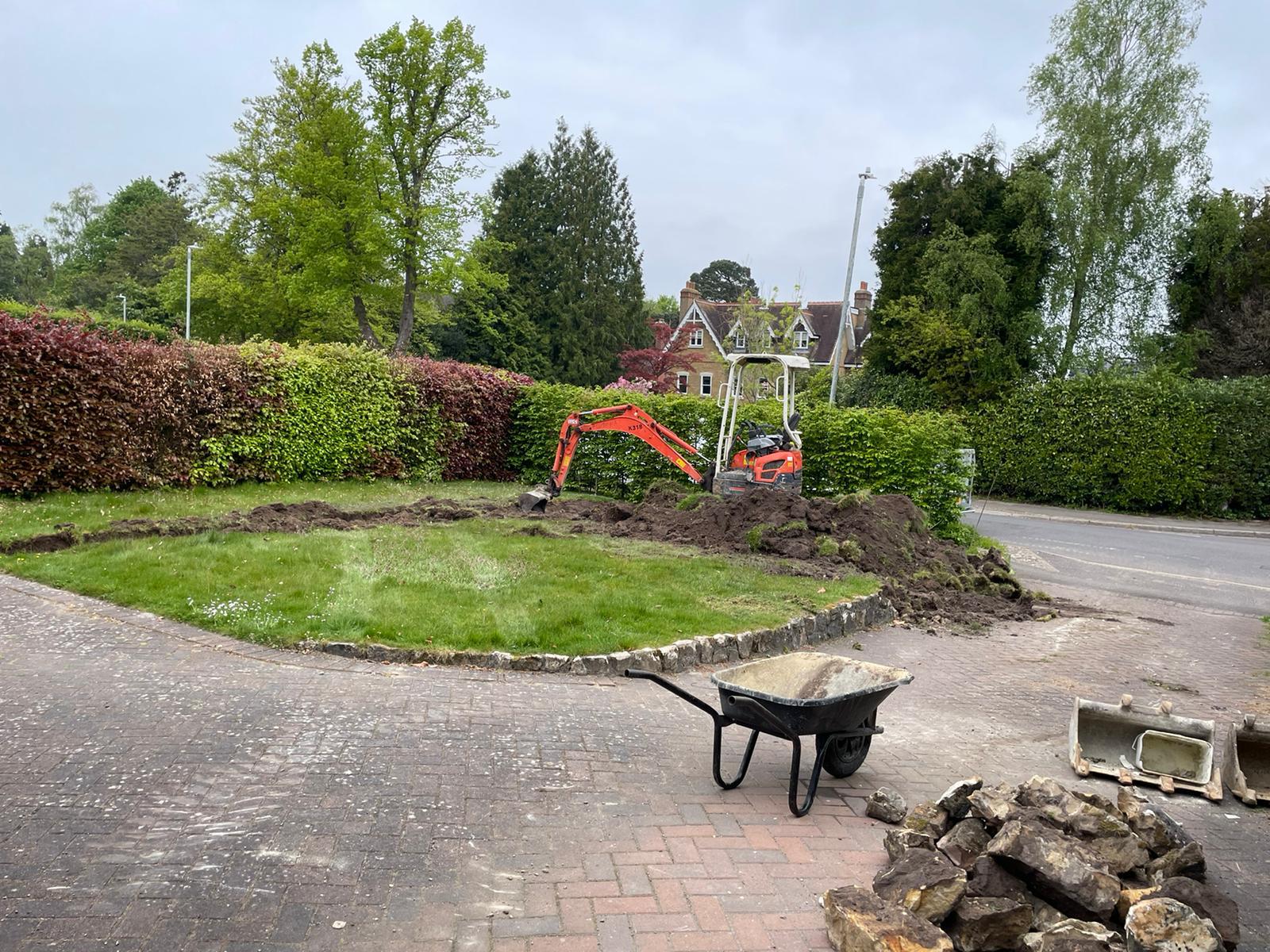 A wheelbarrow is sitting in the middle of a brick driveway next to a pile of rocks.