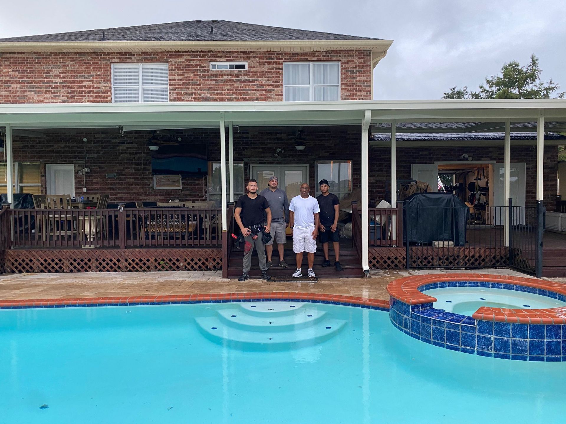 A group of men are standing next to a swimming pool in front of a house.