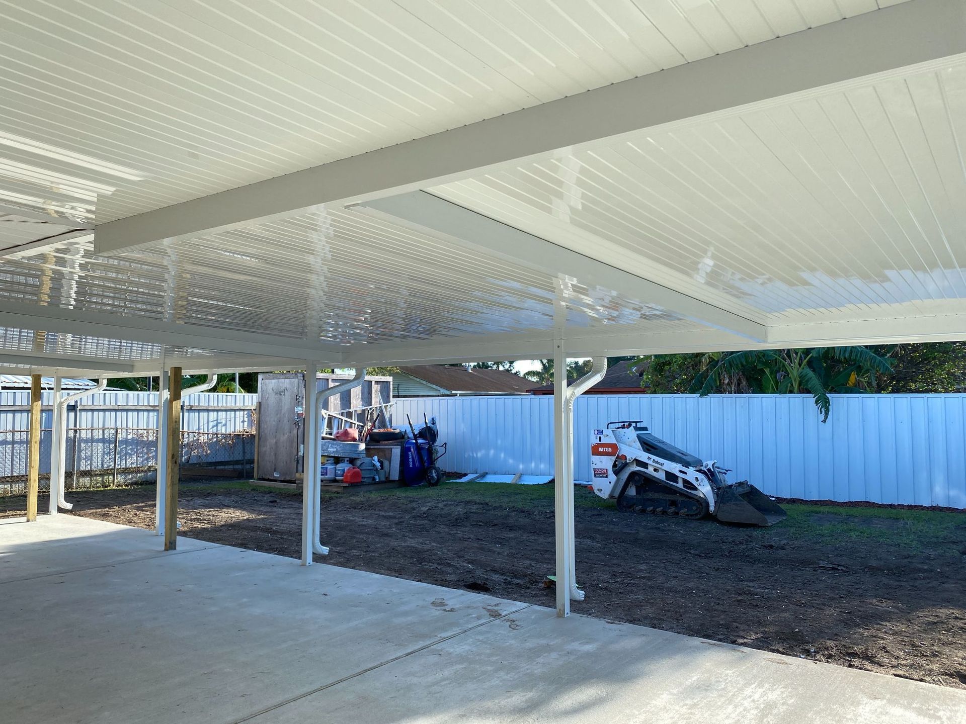 A carport with a white roof and a white fence in the background.