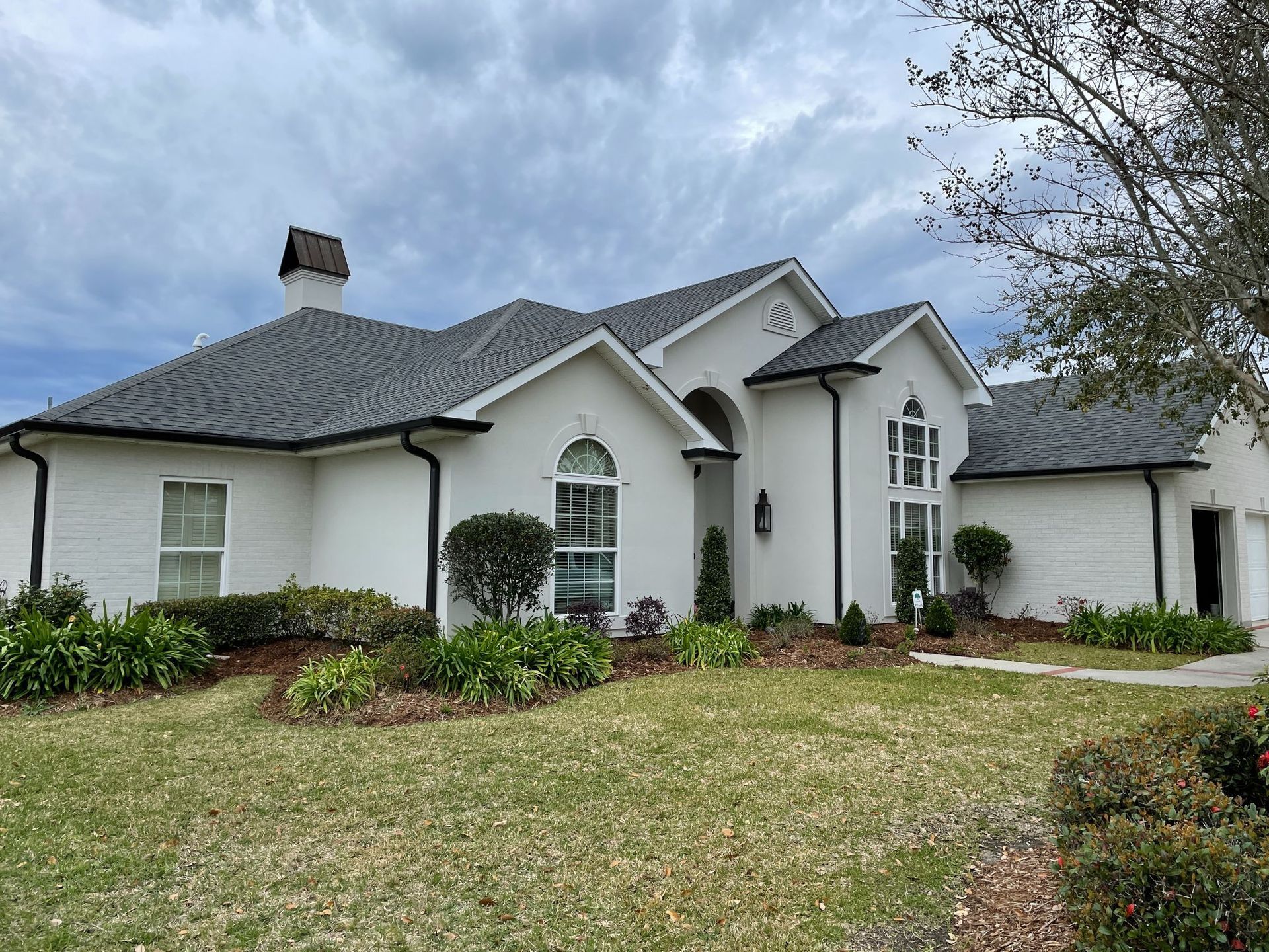 A large white house with a gray roof is sitting on top of a lush green lawn.