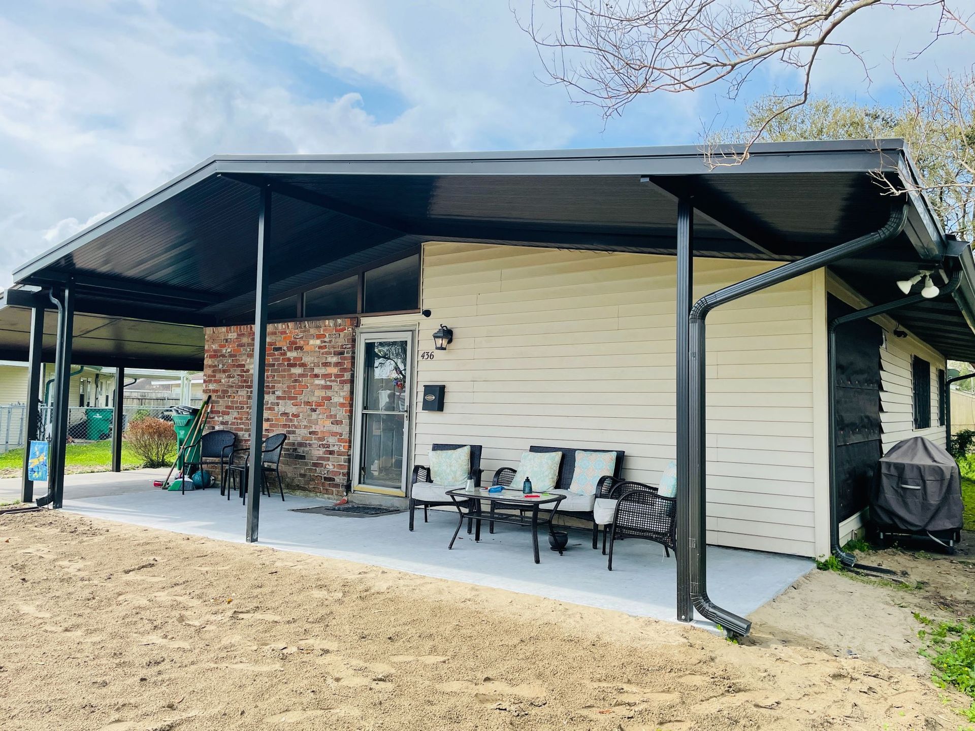 A white house with a black covered porch and patio furniture.