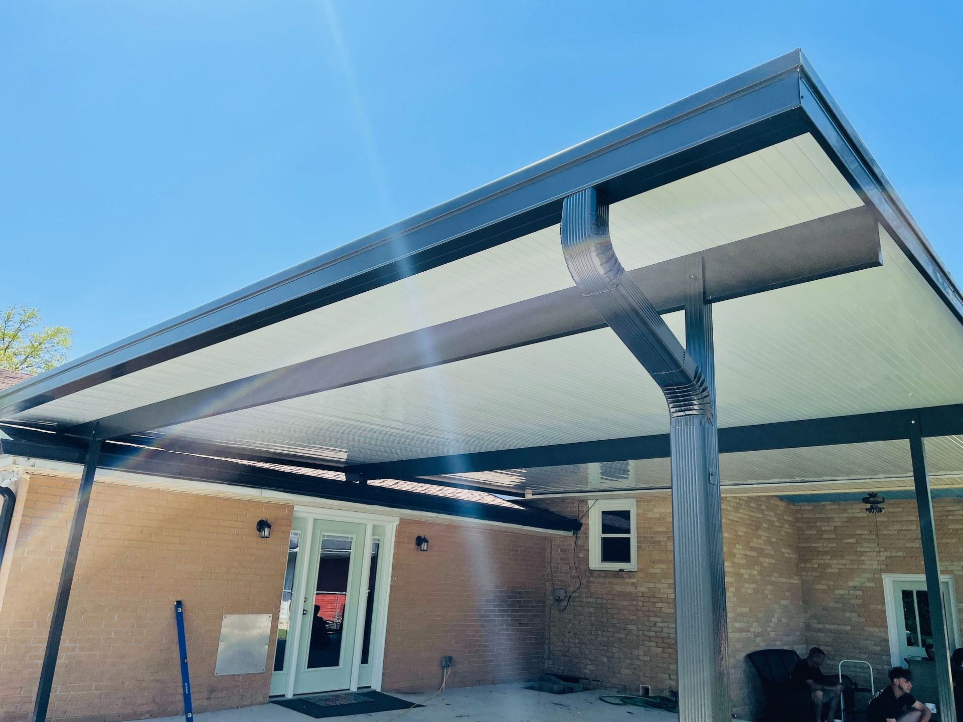 A man is sitting under a covered patio in front of a house.