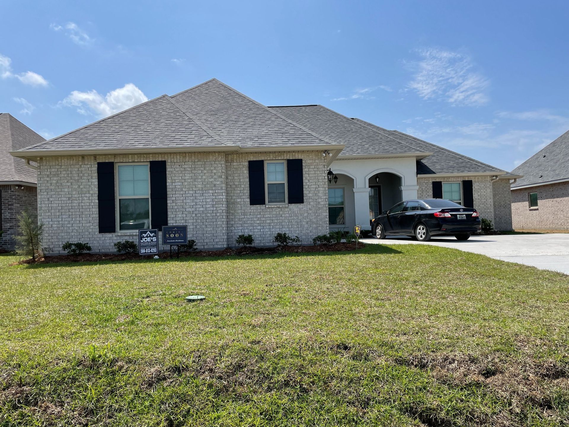 A white brick house with a black car parked in front of it.