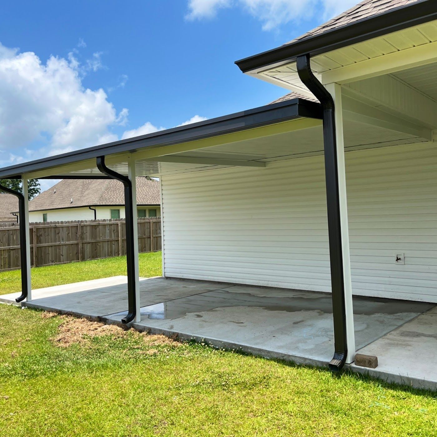 Covered white house patio with concrete slab, dark trim, and a grassy backyard under a blue sky