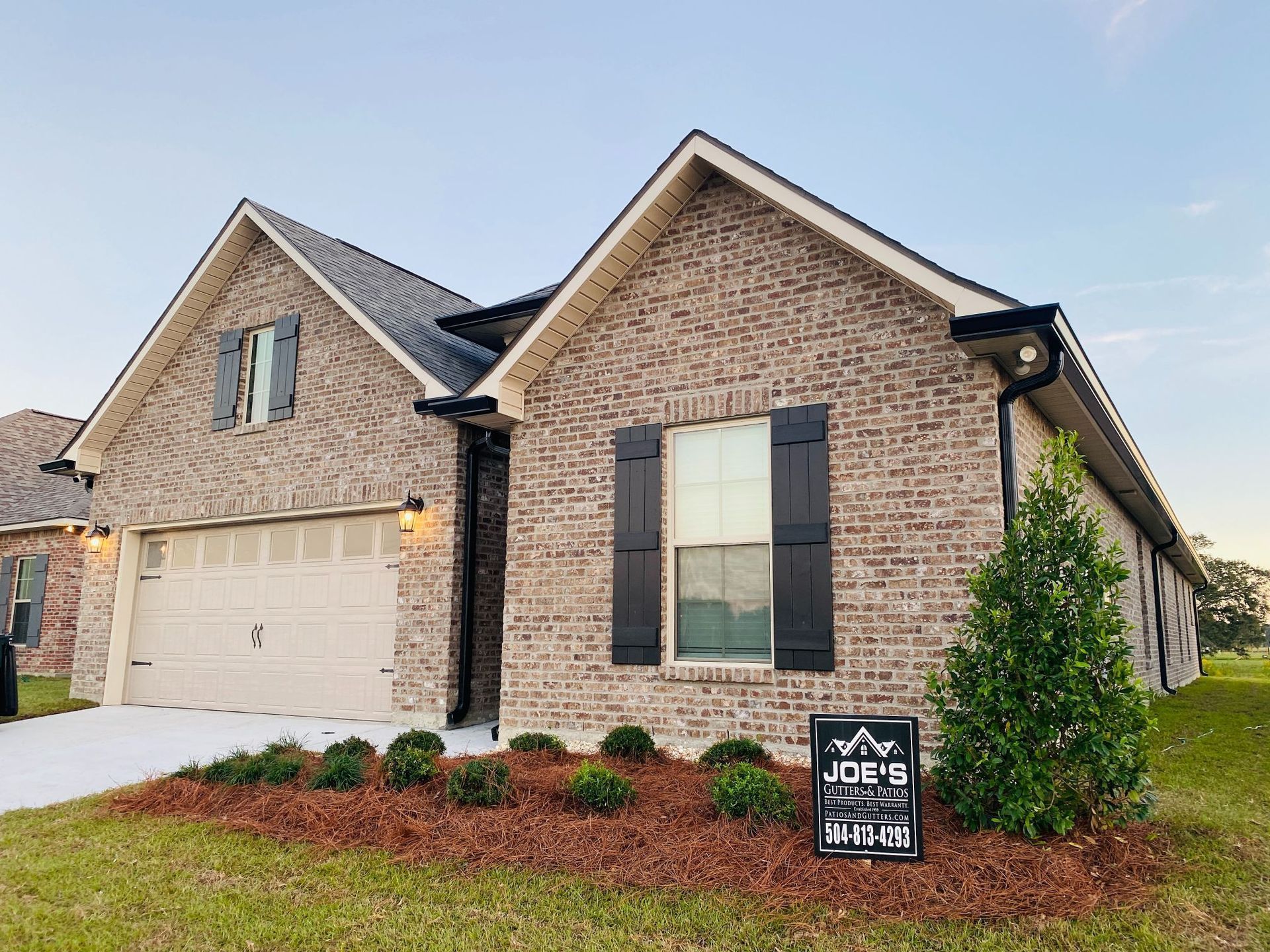 Brick house with black shutters and a garage door, front yard with a sign.