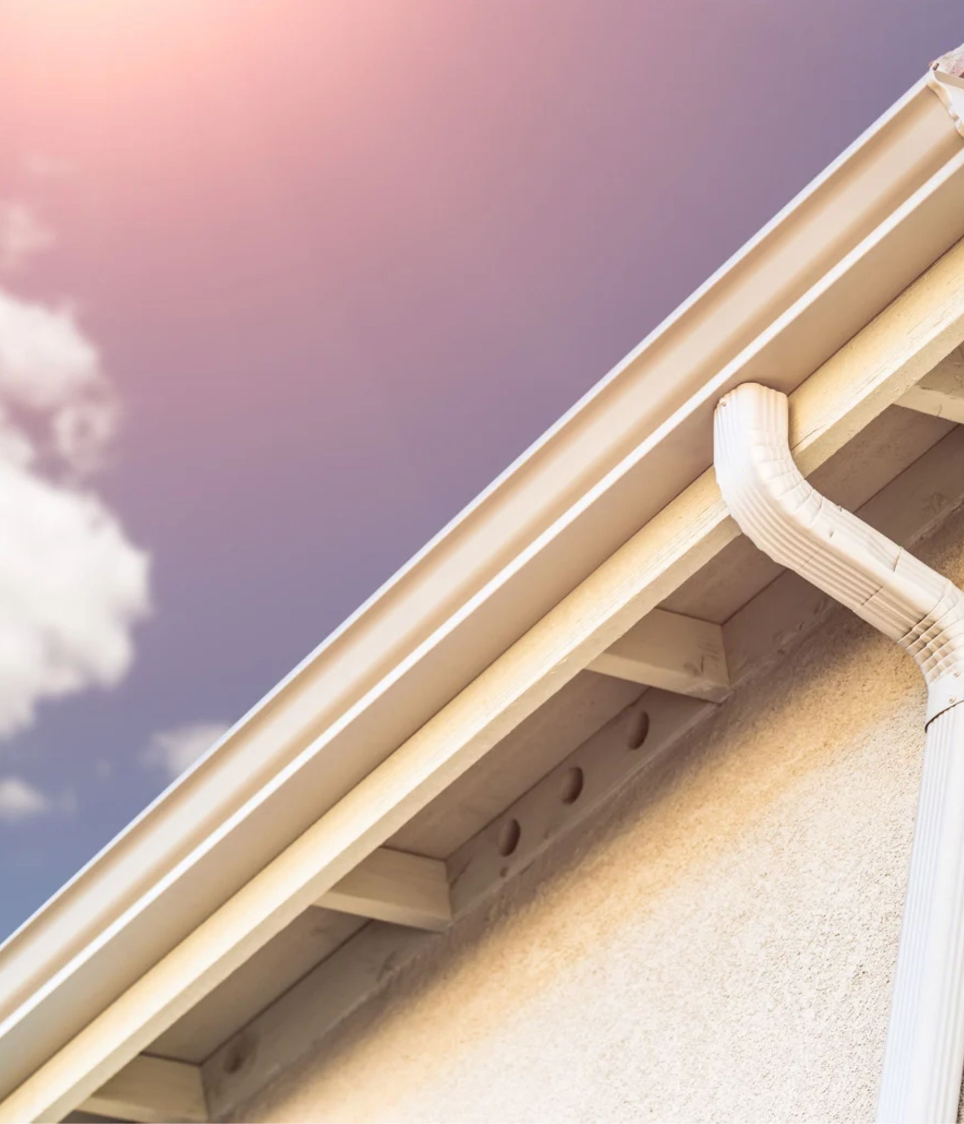 A gutter on the side of a building with a cloudy sky in the background.