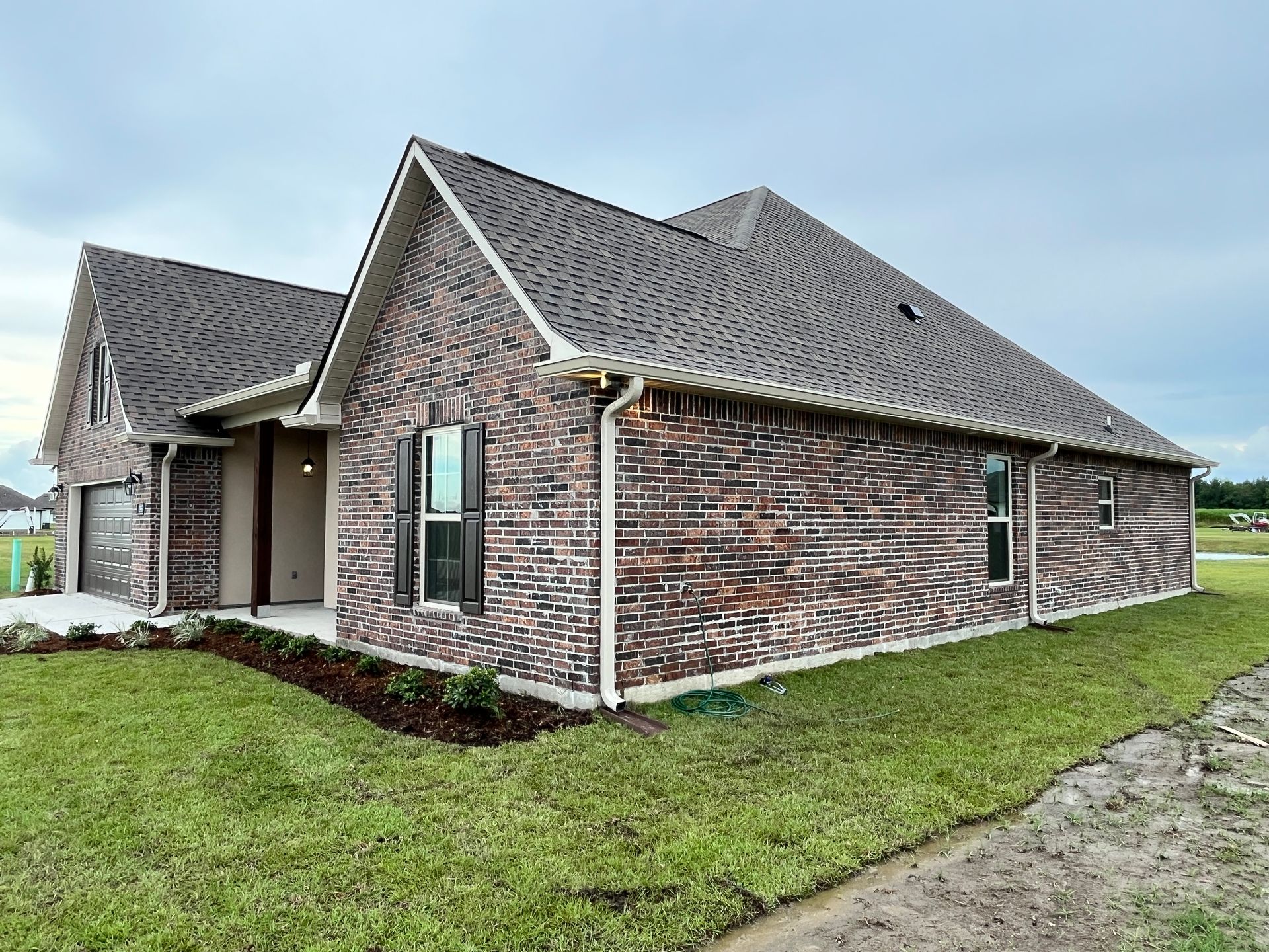 A new, single-story home with dark brown patterned brick, a grey shingled roof, and a side-entry garage on a grassy lot.