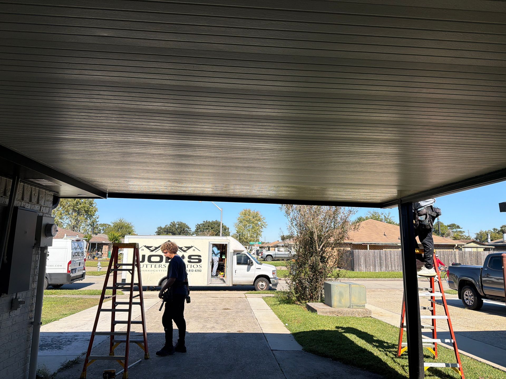 Two workers use ladders to service the underside of an outdoor canopy at a residential home.