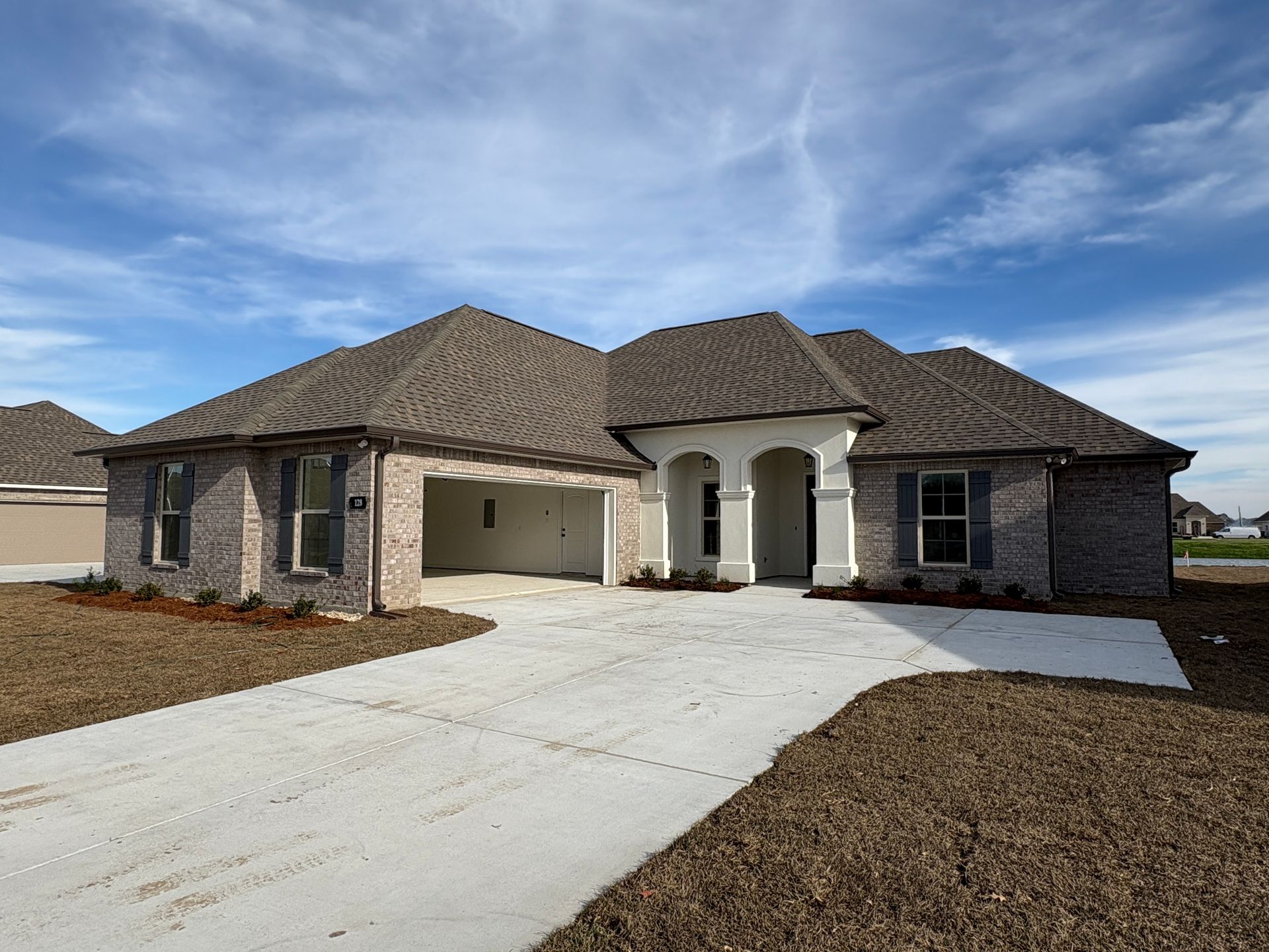 A new single-story house with tan brick, a white arched entry, and a two-car garage under a clear blue sky.