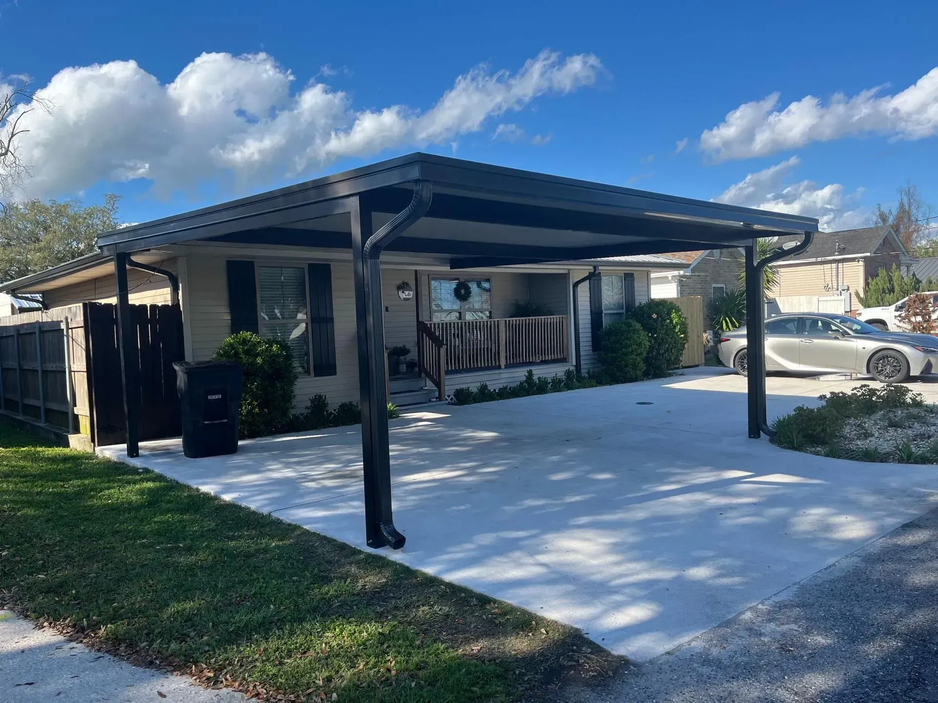Carport beside a house with a fresh white concrete driveway under a blue sky