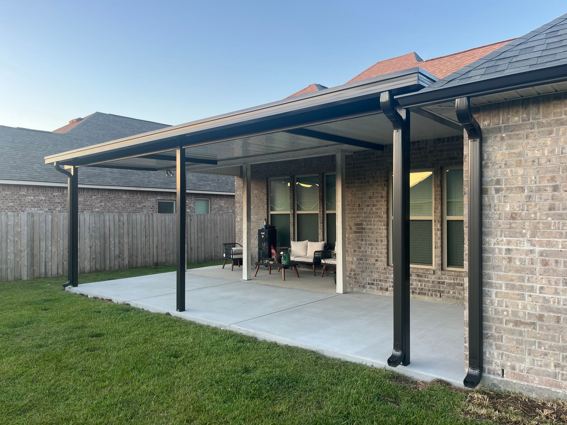 Backyard patio with a large covered porch extension, black support columns, and a concrete floor against a brick house.
