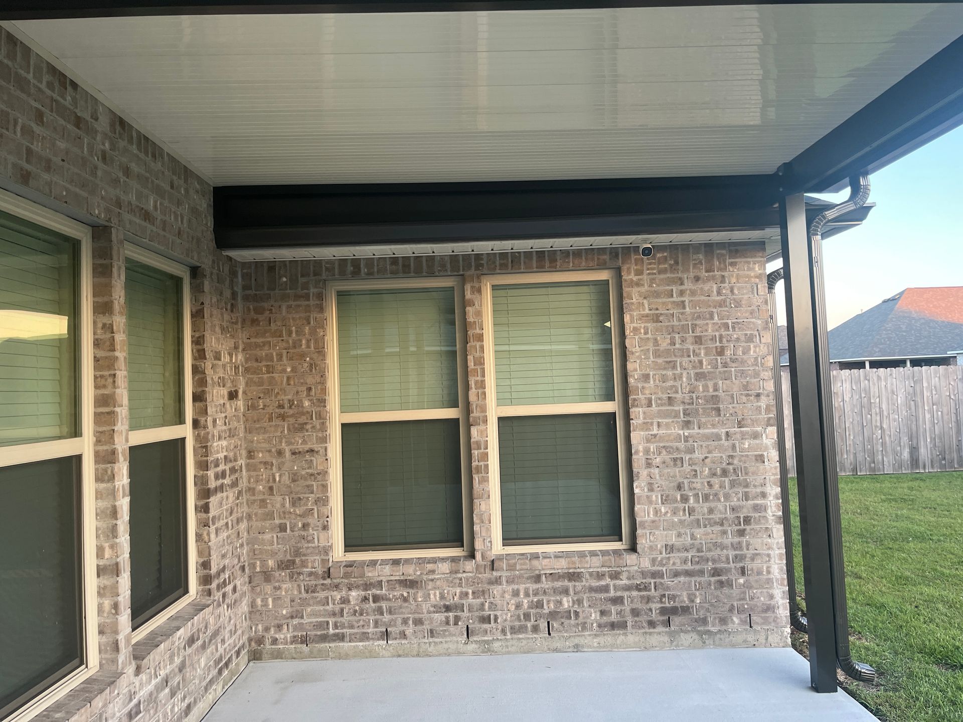 A covered patio with light brick walls, large windows, a white ceiling, and a dark metal support column.