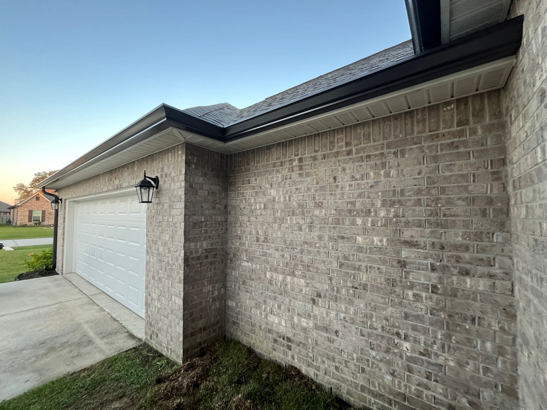 A view of a tan brick house exterior, showing the garage, white garage door, and dark trim under the roof eaves.