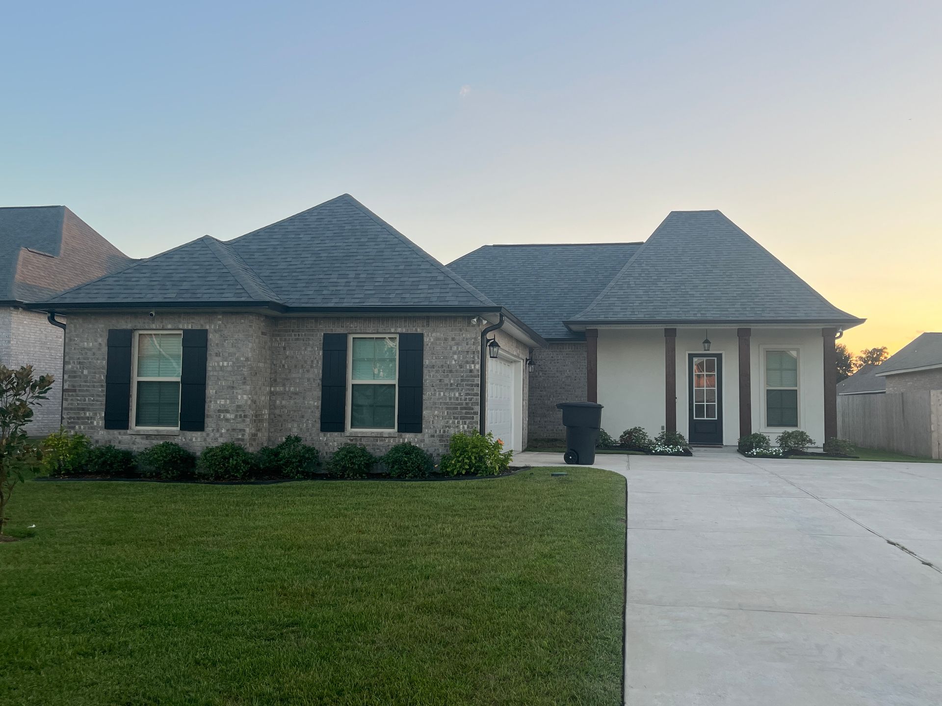 A brick and stucco single-story suburban house with a dark shingled roof, black shutters, and a concrete driveway.