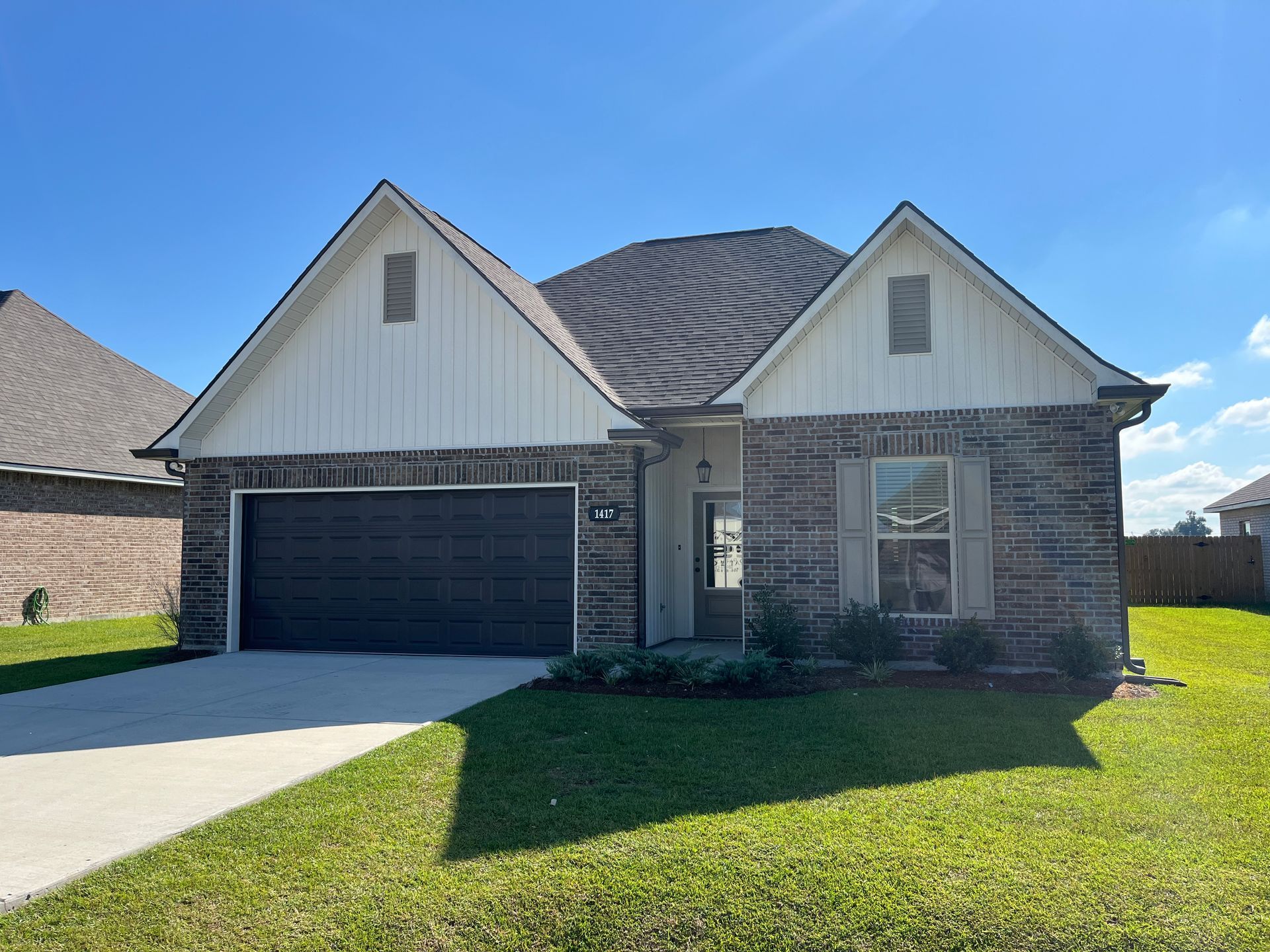 A suburban one-story house with a brick exterior, white siding accents, a dark two-car garage, and a manicured lawn.